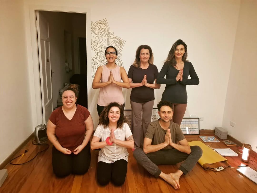 Turma da Casa UM reunida na sala, com as mãos em namastê, diante de uma mandala desenhada na parede